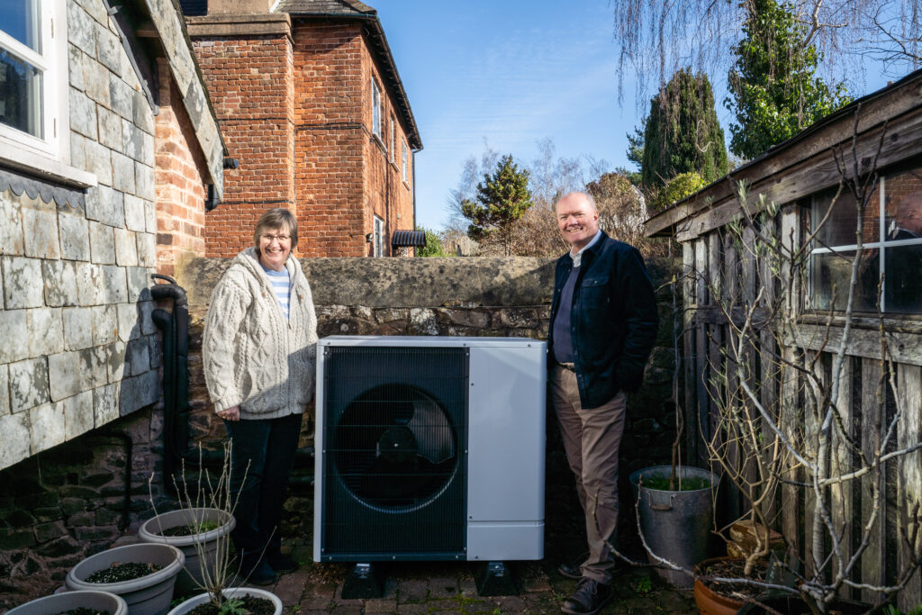 A homeowner in Devon stands outside his house with his new air source heat pump